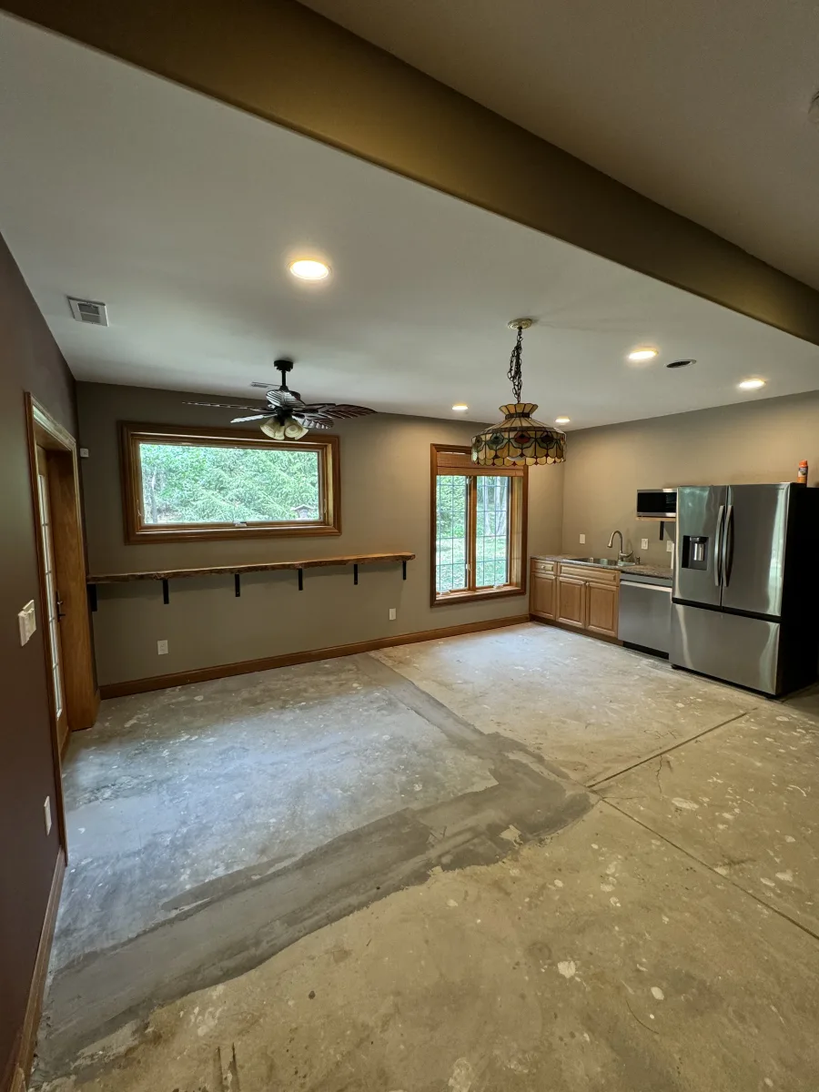 Columbus home addition interior in progress: concrete floor, wood windows, partial kitchenette with stainless steel fridge, recessed lights.