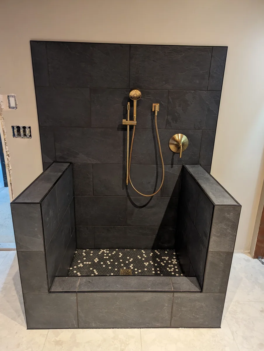Columbus custom dog bathing station: dark slate tile walls, gold shower fixtures, black & white mosaic floor. Expert pet wash.