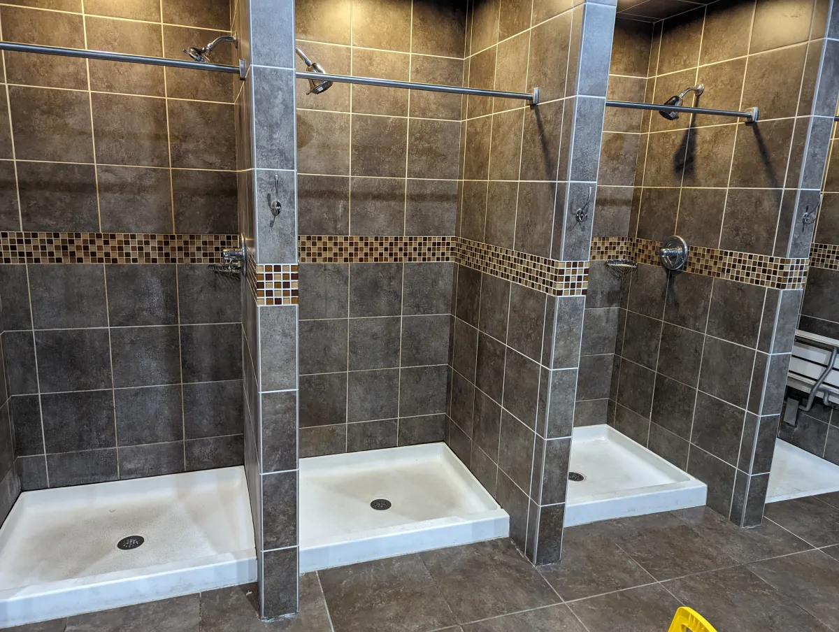 Columbus commercial shower renovation featuring dark brown tiled stalls with mosaic accent, white pans, and chrome fixtures.