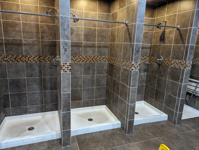 Columbus commercial shower renovation featuring dark brown tiled stalls with mosaic accent, white pans, and chrome fixtures.