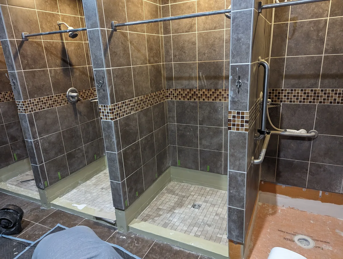 Columbus commercial shower renovation in progress with dark gray wall tiles, mosaic accent, grab bars, and tiled floors.