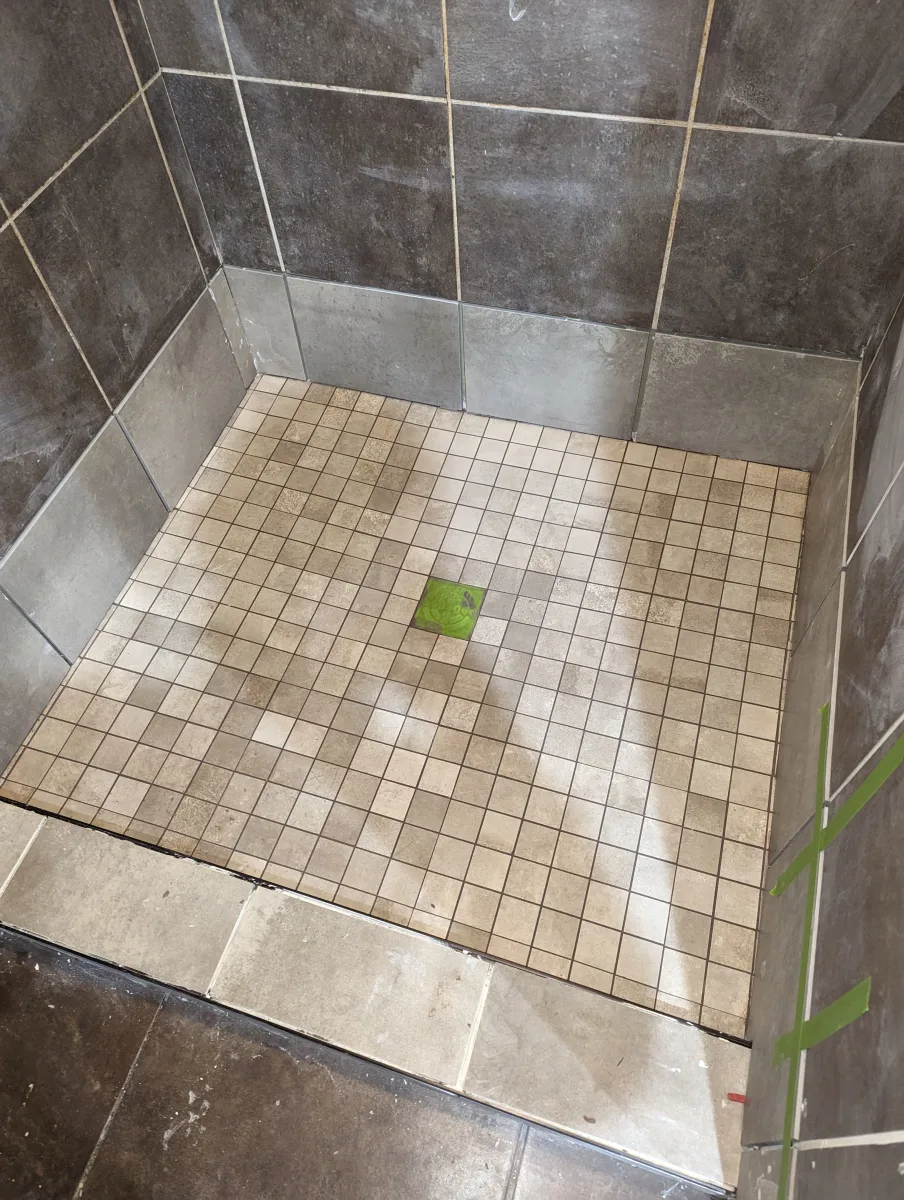 Columbus commercial bathroom remodeling shower with small beige floor tiles, dark wall tiles, and green drain.