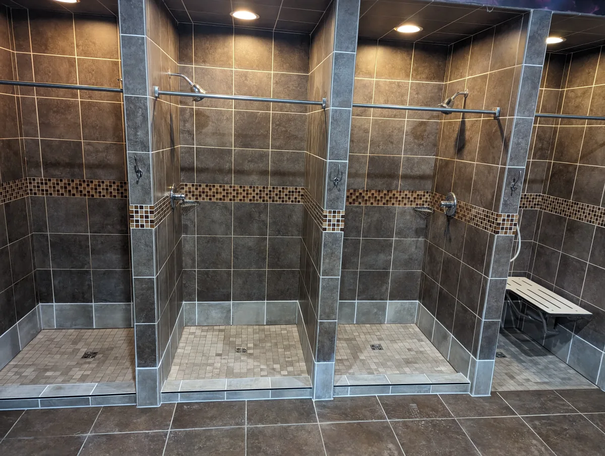 Columbus commercial shower renovation: three modern dark tiled stalls, mosaic accents, light floors, one with accessible bench.