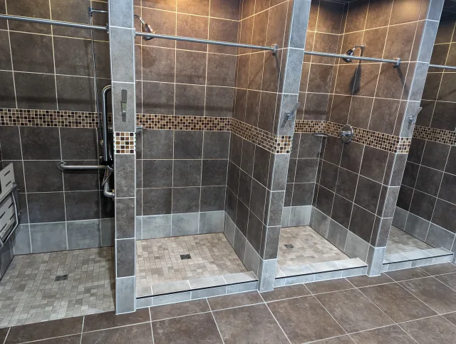 Columbus commercial shower renovation featuring modern dark tiled stalls, mosaic accents, and ADA-compliant grab bars and bench.