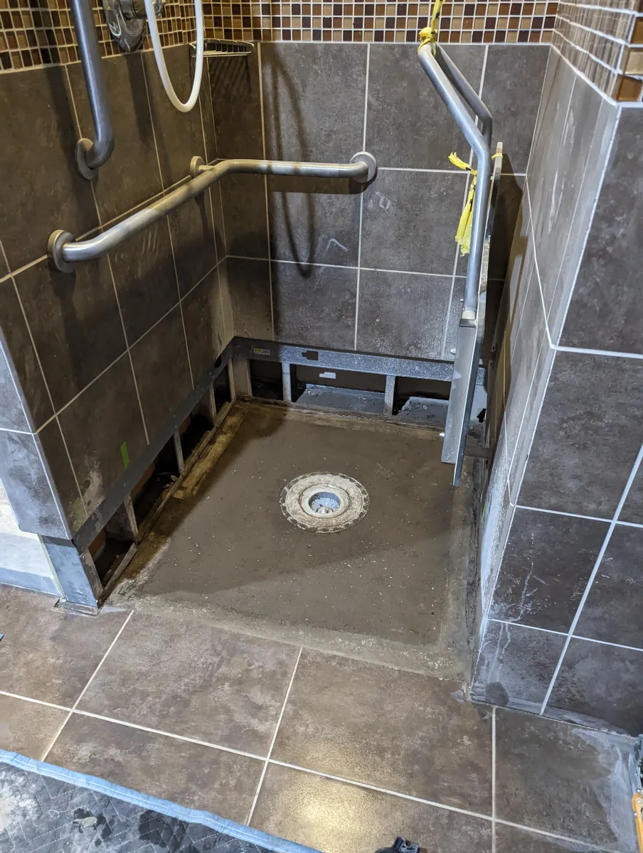 Columbus ADA commercial shower renovation in progress: new concrete base, dark tiles, mosaic accents, and accessible grab bars.