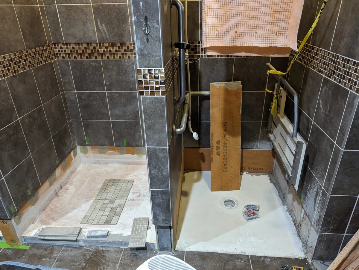 Columbus commercial shower remodel featuring dark tile, mosaic border, Kerdi-Board, and grab bars mid-installation.