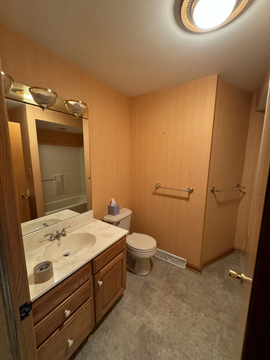 Columbus guest bathroom remodel before. Orange wallpaper, oak vanity, speckled counter, outdated lights & vinyl floor.