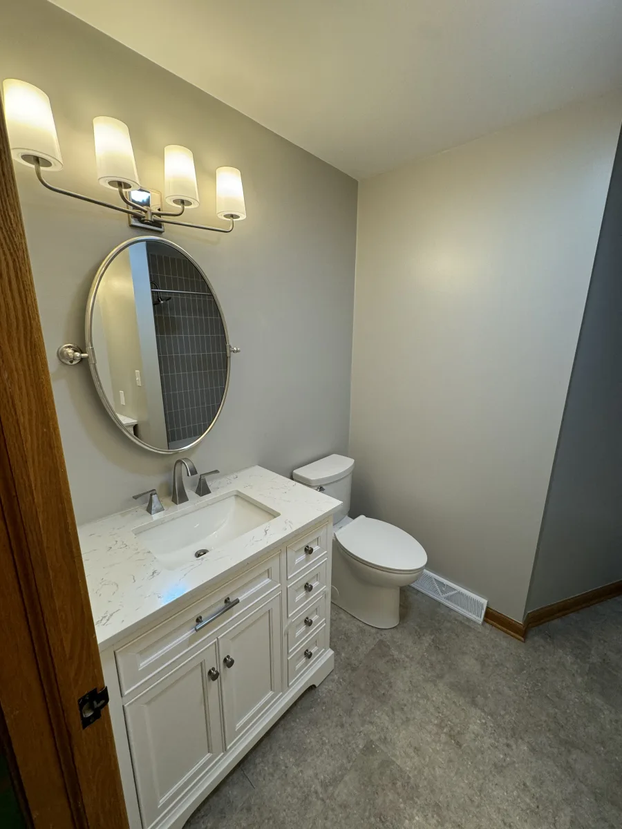Columbus guest bathroom remodel with white vanity, quartz-look counter, oval mirror, and vertical gray subway tile accent.