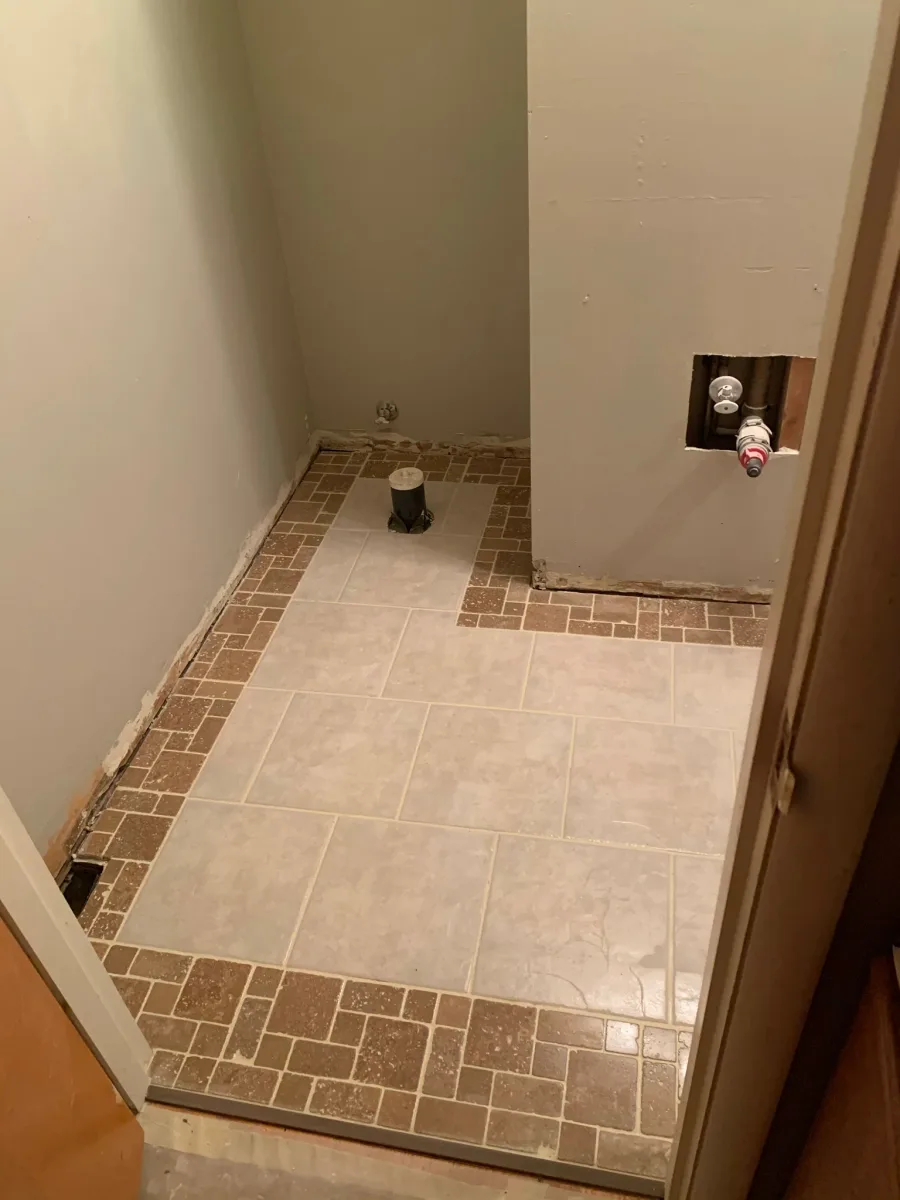 Columbus master bathroom floor tile in progress, showing light beige tiles with a decorative brown mosaic border, by 614 Remodeling Pros.