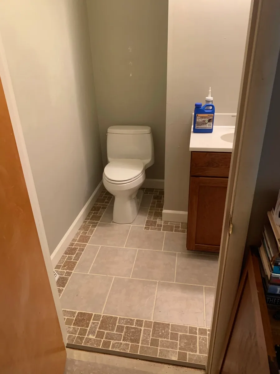 Columbus bathroom remodel: newly installed grey floor tile with mosaic border, white toilet, and dark wood vanity.