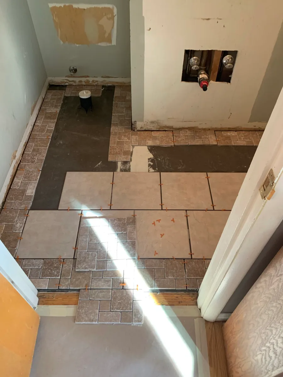 Columbus bathroom tile remodel: floor installation of beige square and rustic brown border tiles in progress.