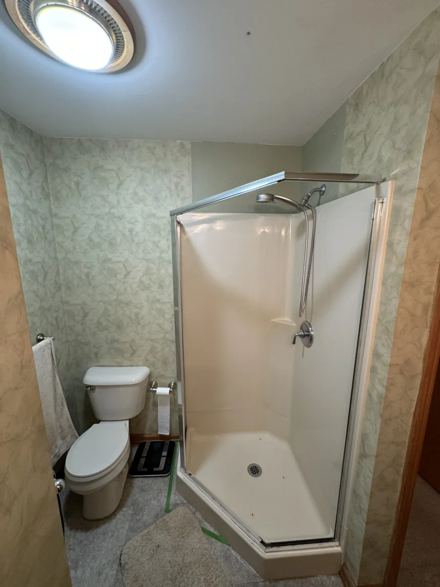 Columbus bathroom remodeling before: old corner shower, standard toilet, green patterned walls, outdated ceiling light.