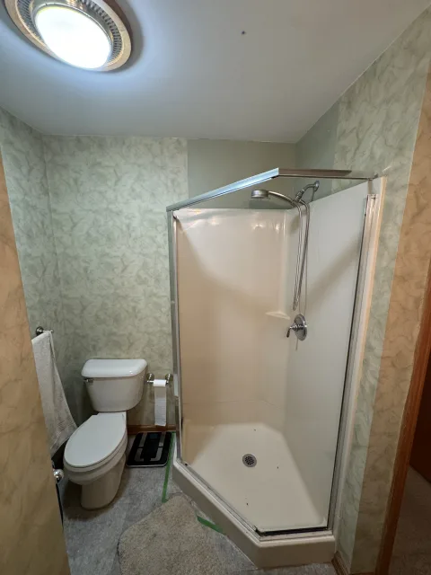 Columbus bathroom remodeling before: old corner shower, standard toilet, green patterned walls, outdated ceiling light.