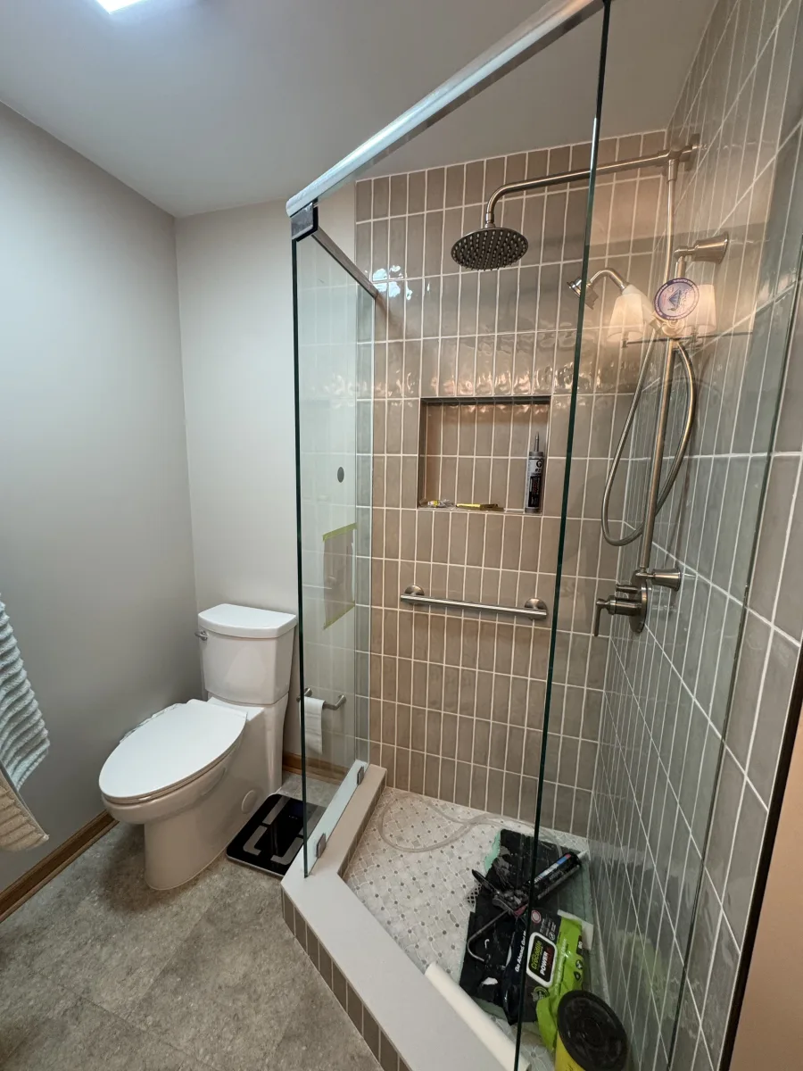 Modern Columbus bathroom remodeling with glass shower enclosure, gray subway tiles, rain head, and white toilet by 614 Remodeling Pros.