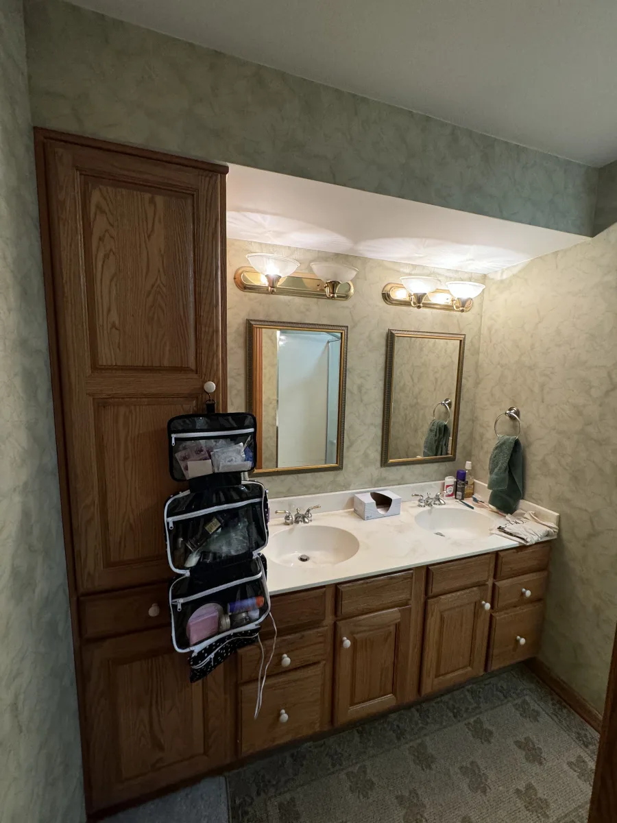 Dated Columbus bathroom before remodel: oak double vanity, cultured marble top, brass lights, green textured walls.