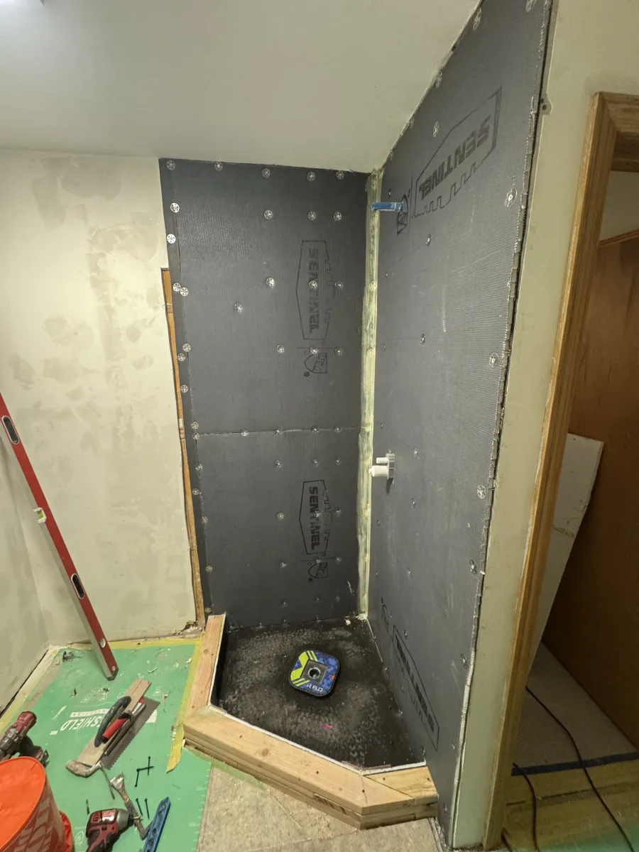 Columbus bathroom remodeling project showing shower waterproofing with black Sentinel panels, pre-sloped pan, and construction tools.